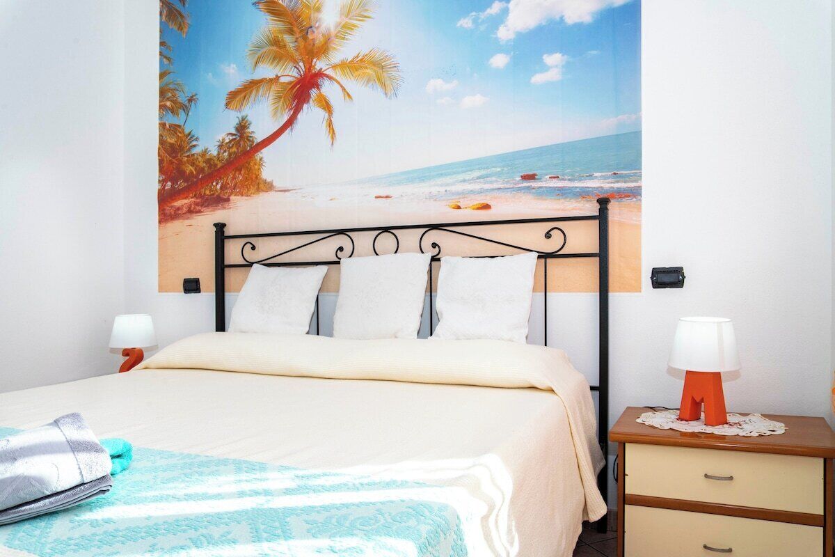 A bed with a beach-themed wall mural, a bedside table with a lamp, and a nightstand with a lamp.