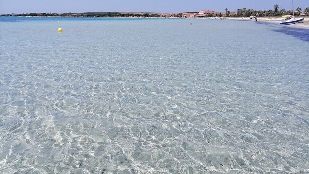 A beach with clear shallow water, a boat on the right, and buildings in the background. - Casa Vanessa by the Sea (Mandriola)