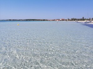A beach with clear shallow water, a boat on the right, and buildings in the background. - Casa Vanessa by the Sea (Mandriola)