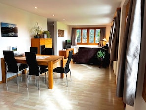 A modern living room with a wooden dining table, black chairs, a sofa, and a TV. - HasliRent, Holiboimi, (Hasliberg Wasserwendi), by Interhome (Hasliberg)