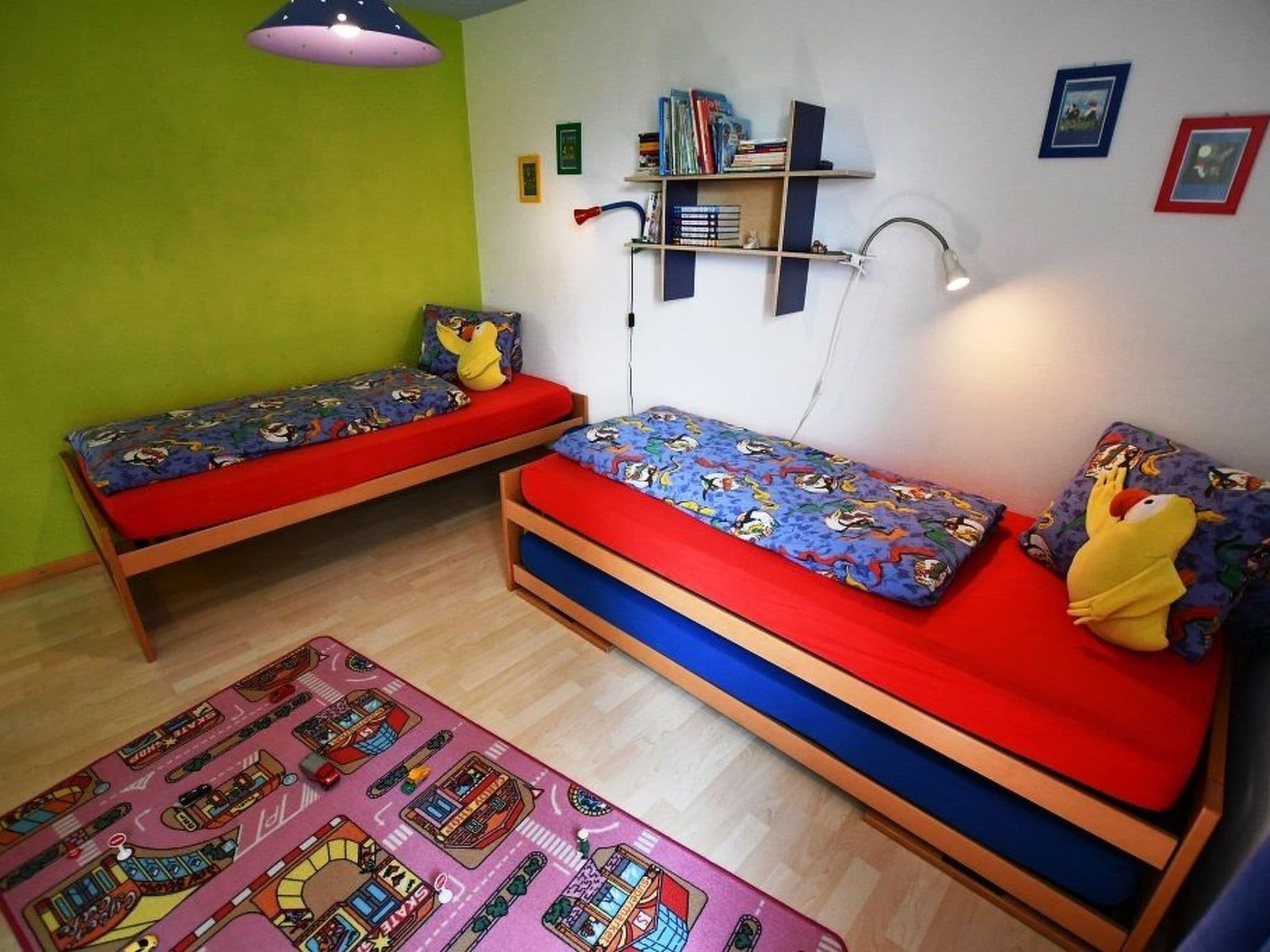 Ein Zimmer mit zwei Etagenbetten, einem Bücherregal, einem Schreibtisch und einem bunten Teppich.