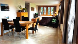 A modern living room with a wooden dining table, black chairs, a dark sofa, and a TV. - HasliRent, Holiboimi, (Hasliberg Wasserwendi), by Interhome (Hasliberg)