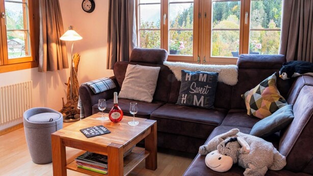 A cozy living room with a brown leather sofa, a wooden coffee table, and a view of a forest through large windows. - HasliRent, Holiboimi, (Hasliberg Wasserwendi), by Interhome (Hasliberg)