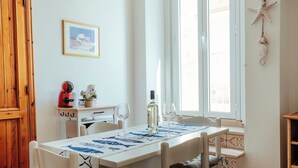 Un coin repas avec une table dressée pour deux personnes, une bouteille de vin blanc et un tableau encadré au mur.