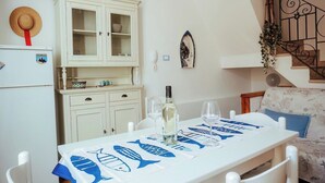 Un coin repas avec une table dressée pour deux personnes, un buffet blanc aux portes vitrées, un réfrigérateur et un escalier doté d’une rampe en fer forgé.