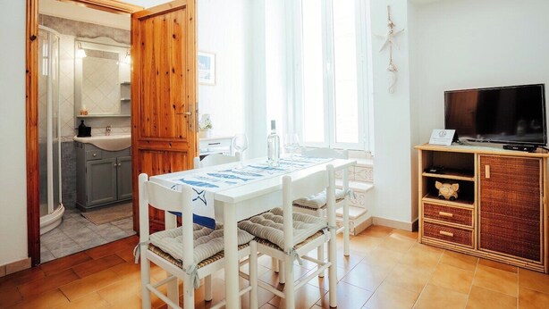 Une pièce comprenant une table à manger, des chaises, un téléviseur, un meuble et une salle de bain visible à travers une porte ouverte.