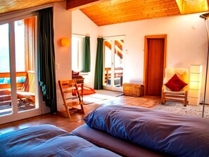 A cozy room with a bed, a chair, a table, and a view through a glass door.