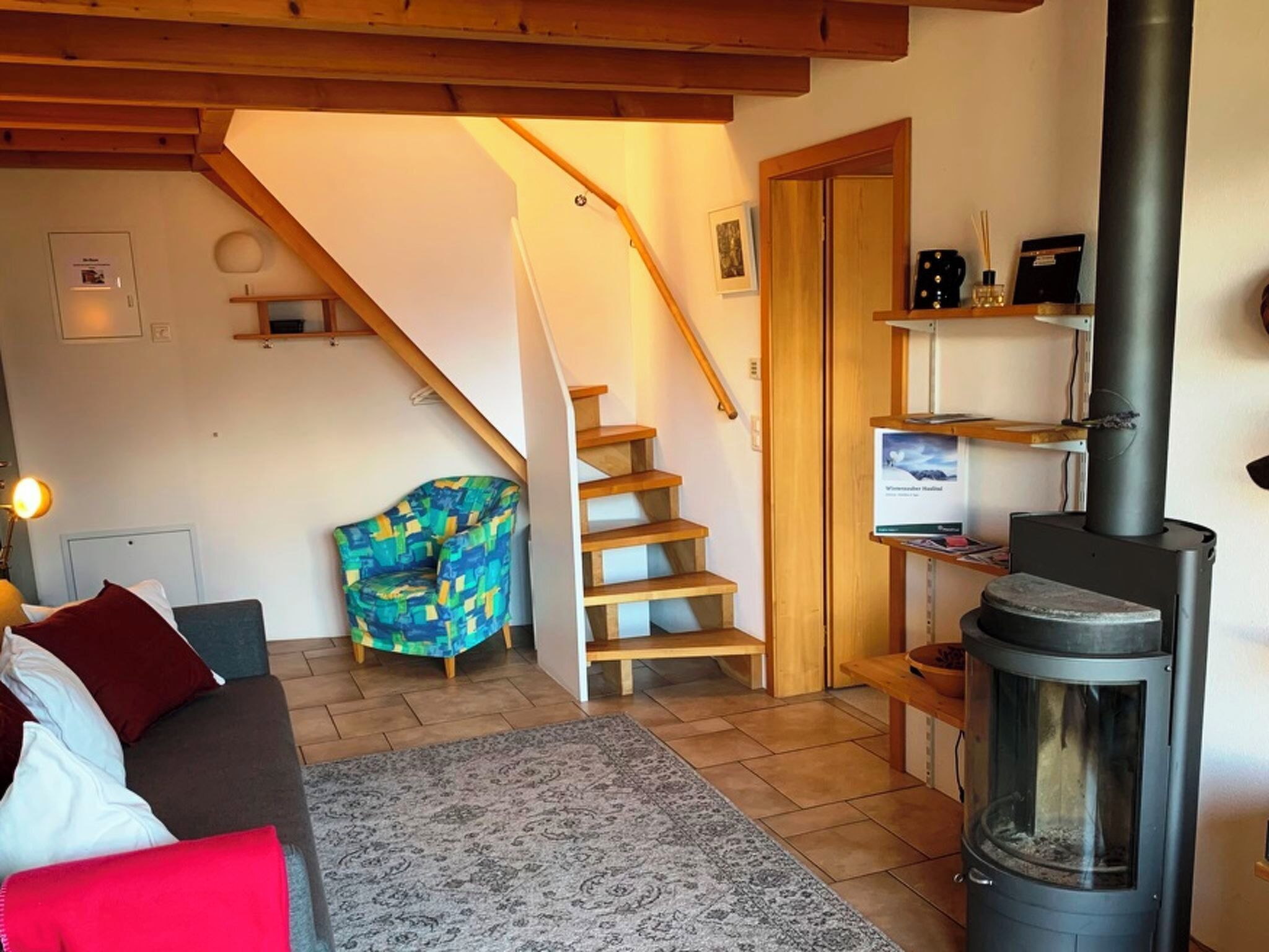Un salon chaleureux avec un canapé, un tapis à motifs, un escalier en bois et un poêle à bois.