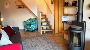 Ein gemütliches Wohnzimmer mit einer Couch, einem gemusterten Teppich, einer Holztreppe und einem Kaminofen.