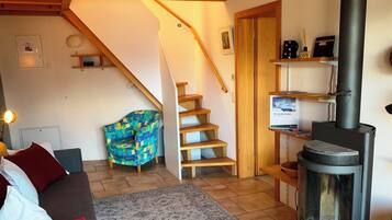 Un salon chaleureux avec un canapé, un tapis à motifs, un escalier en bois et un poêle à bois.