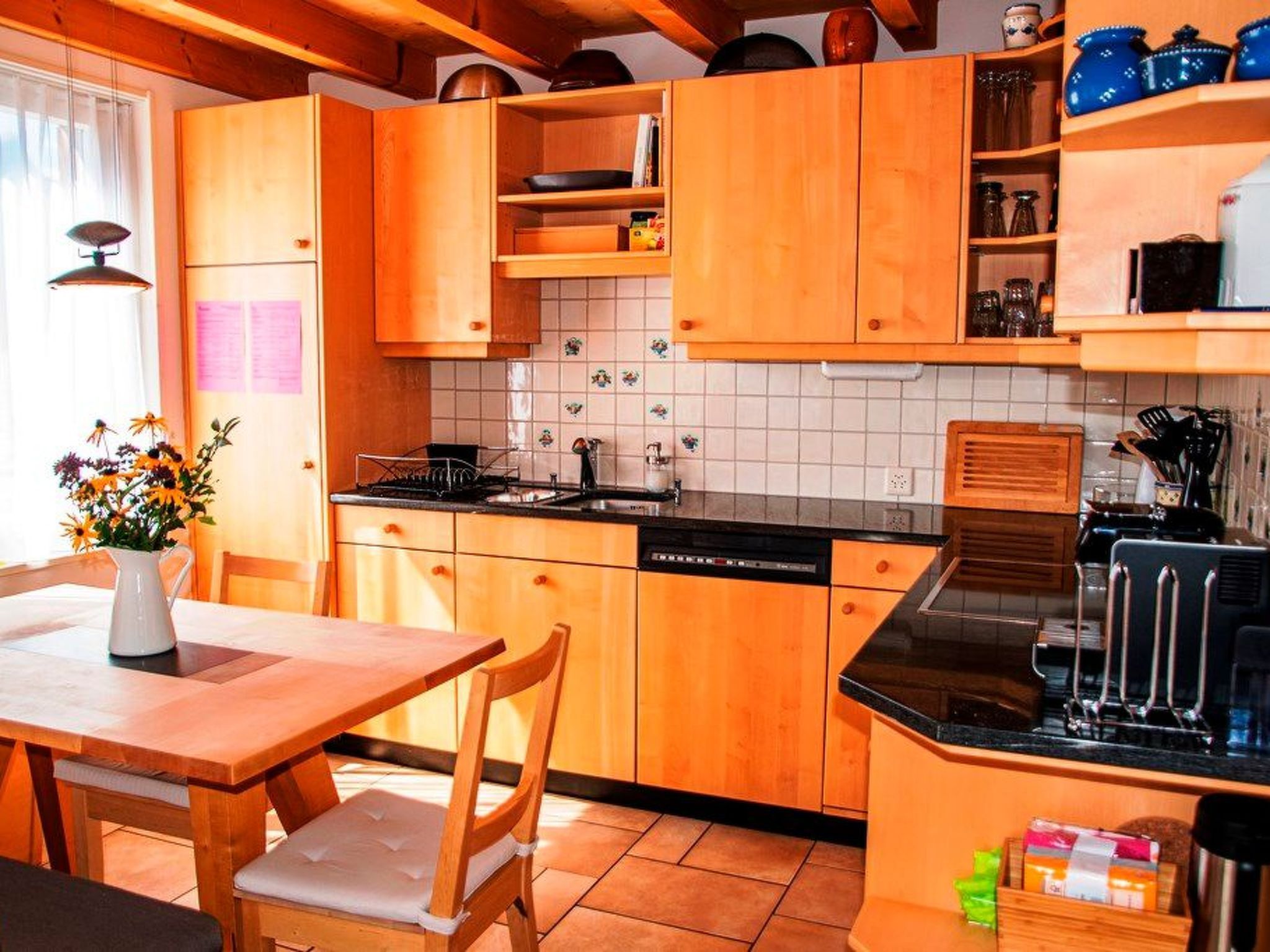Une cuisine avec des meubles de rangement en bois, un plan de travail noir et une table à manger avec des chaises.