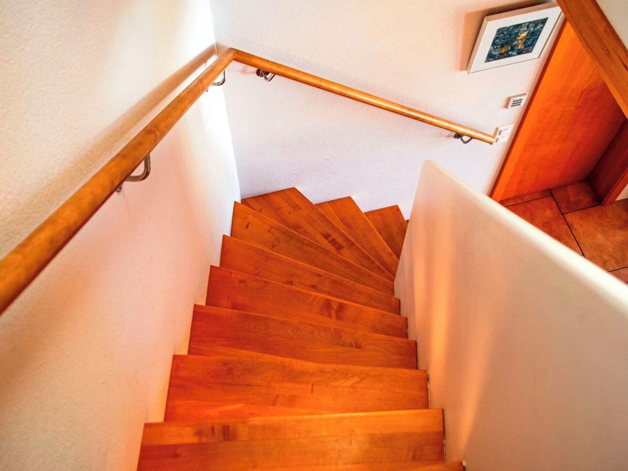 Un escalier en bois avec une rampe, des murs blancs et un tableau accroché au mur.