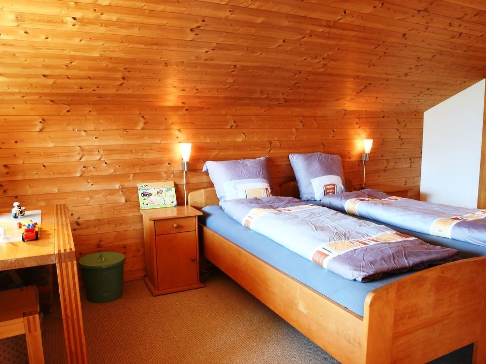Une chambre dans un chalet en bois, avec deux lits, un bureau et une poubelle.