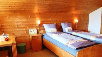 Une chambre dans un chalet en bois, avec deux lits, un bureau et une poubelle.