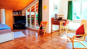 Ein gemütliches Wohnzimmer mit Fernseher, Bücherregalen, einer Holzzieldecke und einem Essbereich mit Stühlen und Tisch.