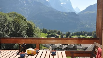 Une terrasse en bois avec une table et des chaises, offrant une vue sur un paysage montagneux parsemé de maisons et de verdure.