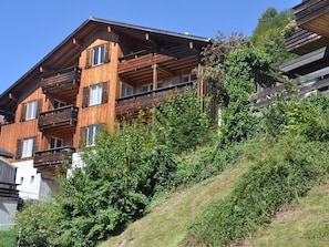 A multi-story wooden building with balconies, surrounded by greenery.