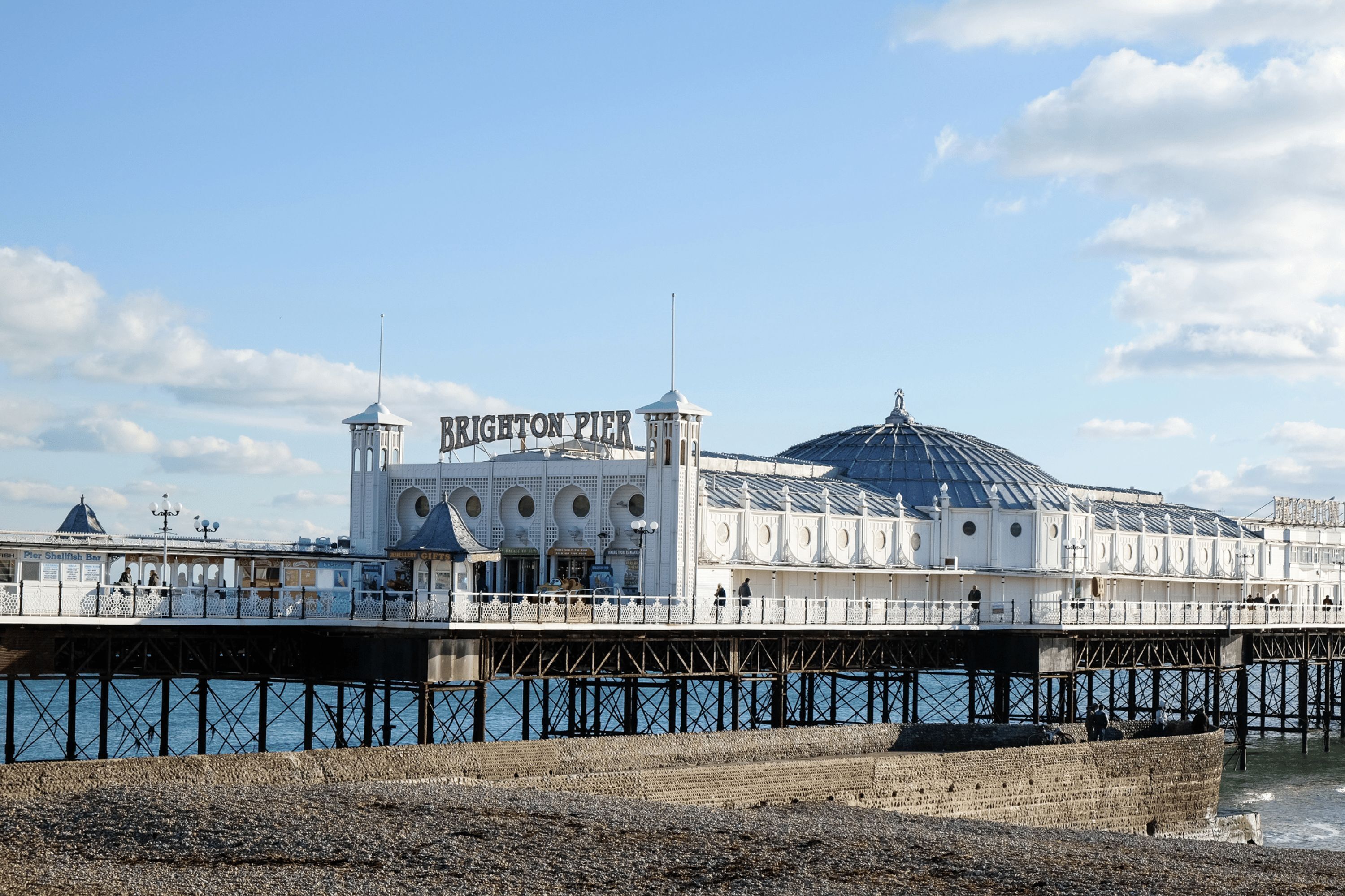 Un muelle con un edificio blanco que tiene una cúpula y un letrero que dice 'Brighton Pier'.
