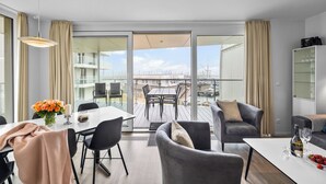 Una sala de estar moderna con comedor, ventanas amplias y un balcón con mobiliario exterior.