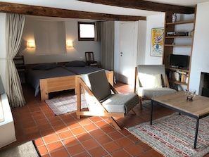 Een gezellige kamer met een bed, twee stoelen, een tafeltje, een boekenkast en een raam.