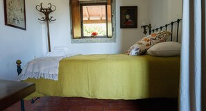 Een kamer met een bed, een raam met uitzicht, een kapstok en een aan de muur hangend schilderij.