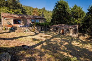 A rustic stone house with a tiled roof, a patio with outdoor furniture, and a garden area. - Stone house with ocean views (A Guarda)