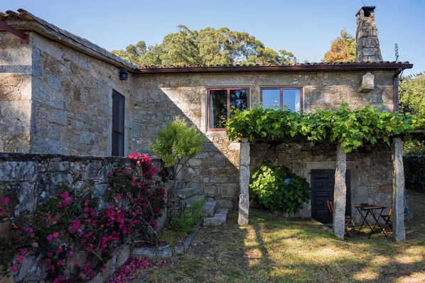 A stone building with a small garden area, a door, and a window.