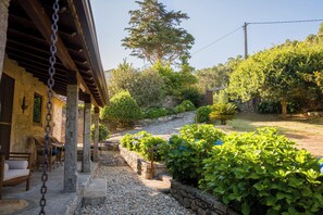 Een landelijk stenen gebouw met een overdekte veranda en een grindpad dat naar een tuin leidt.