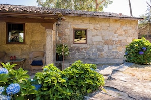 A stone building with a tiled roof, a wicker chair, and a small table with two red lanterns.