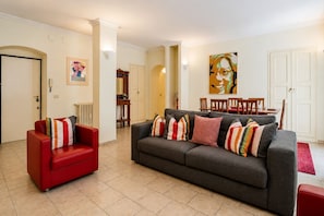 A living room with a grey sofa, red armchair, and a dining table with chairs. - Dama Apartment Prati (Roma)