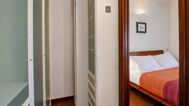 A bedroom with a bed, a nightstand, and a wall-mounted light fixture. - Dama Apartment Prati (Roma)