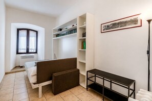 A compact bedroom with a bed, a sofa, a bookshelf, and a framed picture on the wall. - Dama Apartment Prati (Roma)
