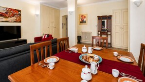 A dining area with a wooden table set for four, a red runner, and a television in the background. - Dama Apartment Prati (Roma)