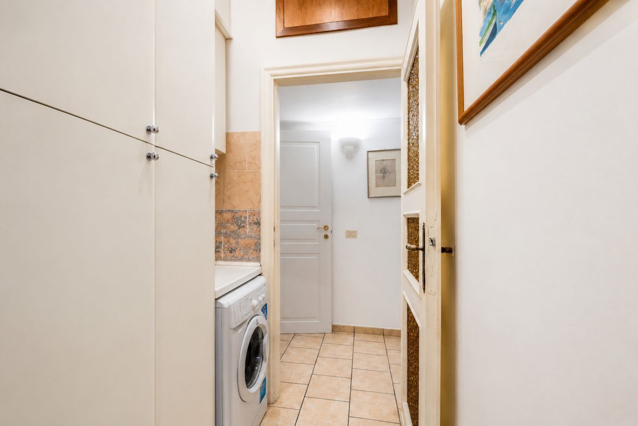 A laundry room with a washing machine, a door leading to another room, and a wall-mounted picture frame.