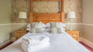 A neatly made bed with a wooden headboard, two bedside tables with lamps, and patterned wallpaper.
