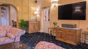 A room with a patterned sofa, a wooden cabinet, a television mounted on the wall, and a small table with a plant.