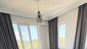 Uma sala de estar moderna com um sofá cinzento, uma mesa de jantar com cadeiras, um tapete cinza e janelas grandes com cortinas.