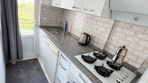 Uma cozinha moderna com armários brancos, bancada de granito, fogão a gás, forno e uma janela com cortinas.