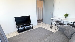 Uma sala de estar moderna com sofá, televisão e área de jantar com cadeiras e mesa.