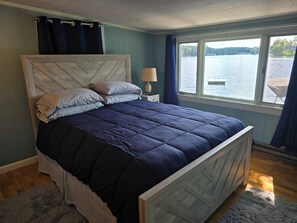 Un dormitorio con cama, mesita de noche, lámpara, ventana y vista al lago, además de un cabecero de madera.
