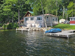 Una cabaña junto al lago con un muelle, un bote y una silla.