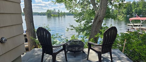 Two Adirondack chairs facing a lake with boats and a dock in the background.