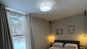 Ein Schlafzimmer mit einem Bett, einem Fenster mit Vorhängen, einer Heizung und Wandleuchten.