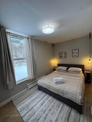 Ein Schlafzimmer mit einem Bett, einem Fenster mit Vorhängen, einer Heizung und Wandleuchten.