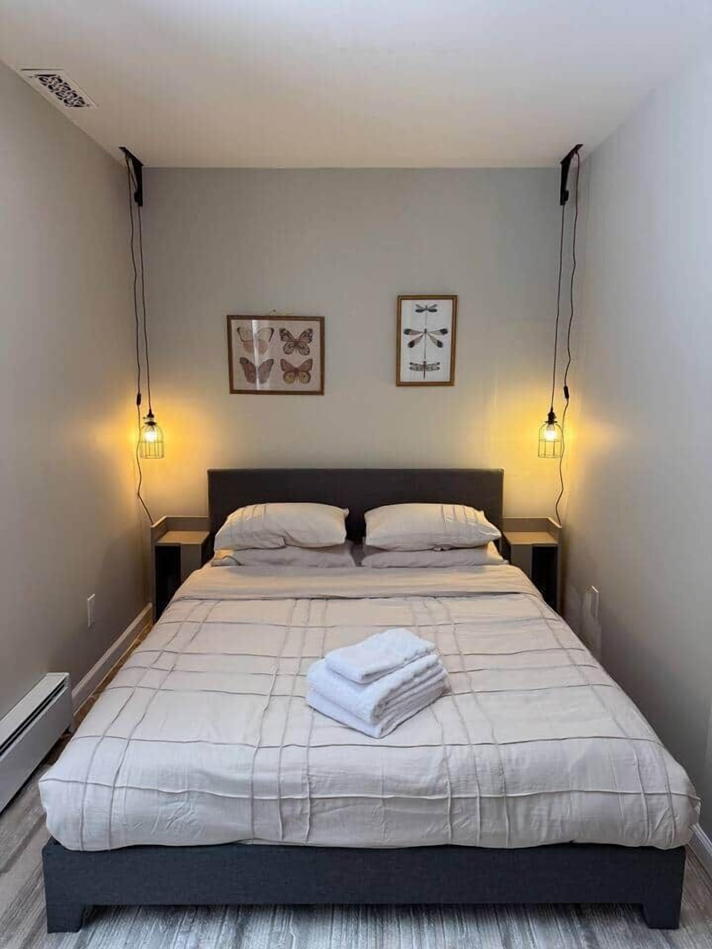 A neatly made bed with a quilt, two wall-mounted lamps, and two framed pictures on the wall.