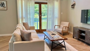 Una sala de estar con sofá, sillón, mesa de centro y televisor sobre un mueble.