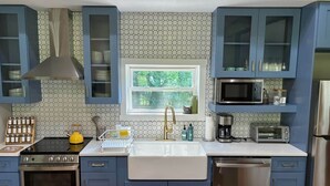 Una cocina con armarios azules, estufa de acero inoxidable, lavamanos con grifo dorado, microondas y lavavajillas.