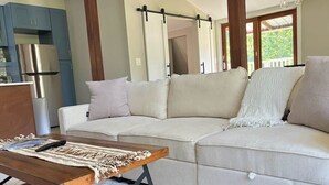 Una sala de estar con sofá, una mesa de centro de madera y una zona de cocina con armarios y electrodomésticos.