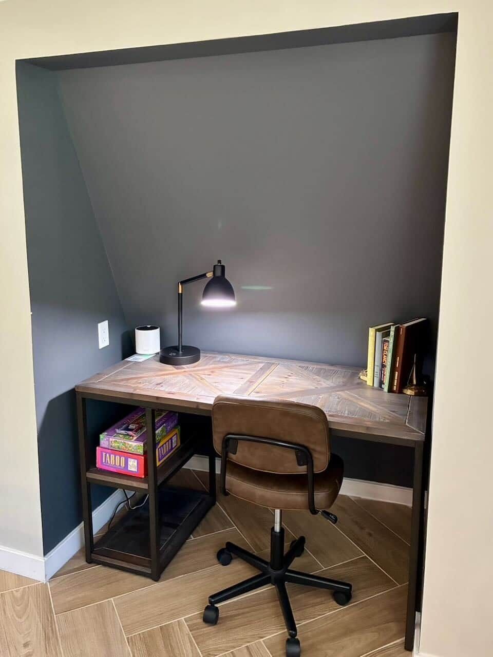Un espacio de trabajo con escritorio, silla, lámpara, libros y estantería con cajas.