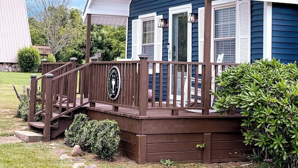 A blue house with a porch, a wooden deck, and a sign.